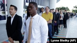 FILE - Luis Mendez, left, a student at Miami Dade College, left, and Maurice Mike, a student at Florida International University, wait in line at a job fair held by the Miami Marlins, at Marlins Park in Miami in 2013.
