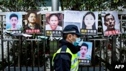 FILE - A police officer walks past placards of detained rights activists taped on the fence of the Chinese liaison office in Hong Kong, Feb. 19, 2020.