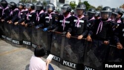 An anti-government protester sits on the ground praying in front of a line of Thai police near Government House in Bangkok, Feb. 14, 2014.