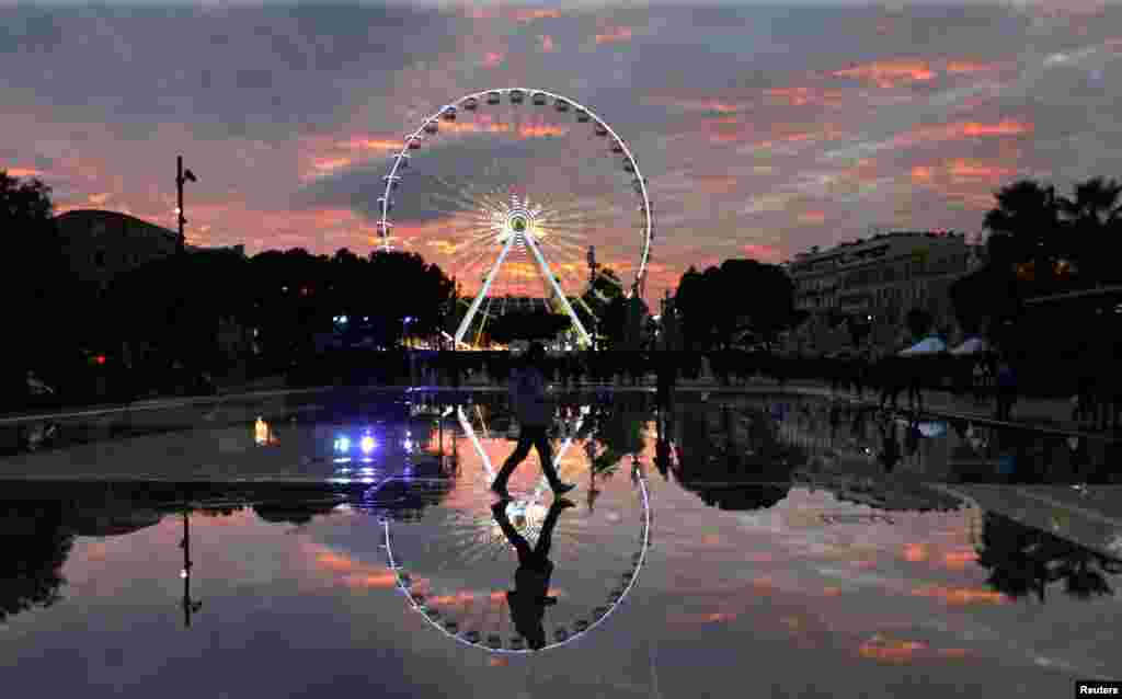 Bayangan dari seorang pria dan wahana hiburan kereta gantung &quot;Ferris wheel&quot; di kota Nice, Perancis.