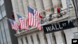 ປ້າຍ​ຖະ​ໜົນ Wall Street ແລະ ທຸງ​ຊາດ​ສະ​ຫະ​ລັດ ປັກ​ຢູ່ນອກ​ຕຶກ​ຂອງ​ຕະຫຼາດ​ແລກ​ປ່ຽນ​ຮຸ້ນ ນິວຢອກ, ນະ​ຄອນ ນິວຢອກ, 3 ມັງ​ກອນ 2020.