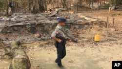 FILE - A Myanmar security officer walks past burned Rohingya houses in Ka Nyin Tan village of suburb Maungdaw, northern Rakhine state of western Myanmar, Sept. 6, 2017.
