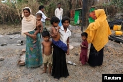 FILE - A family stands beside remains of a market which was set on fire, in Rohingya village outside Maungdaw, in Rakhine state, Myanmar, Oct. 27, 2016. HRW says Myanmar's new government has “not capitalized on its initial momentum in guiding the country toward substantive reform or the creation of democratic institutions.”