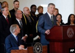 FILE - Texas Governor Greg Abbott, lower left, listens as Dallas Mayor Mike Rawlings, right, address the media during a news conference at city hall, in Dallas, July 8, 2016.