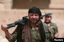 FILE - A Kurdish fighter from the People's Protection Units (YPG) carries his weapons as he walks along a street in the northeastern city of Hasaka, Syria, Aug. 21, 2016.