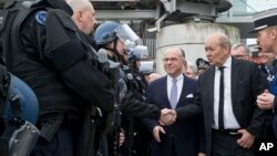 Le ministre français de la Défense Jean-Yves Le Drian, au centre, et le son homologue de l'Intérieur Bernard Cazeneuve, 2e à droite, saluent des policiers français lors d’une inspection des mesures de sécurité à l'aéroport Charles de Gaulle, à Roissy, au nord de Paris, 23 mars 2016.