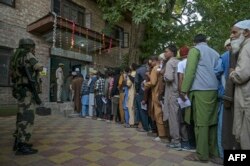 FILE - An Indian security personnel stands guard as voters queue up to cast their ballots at a polling station during the first phase of assembly elections in Pulwama, south of Srinagar on Sept. 18, 2024.