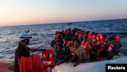 Seorang anggota kelompok LSM "Sea-Watch" memberikan jaket pelampung kepada para migran Afrika yang berdesakan menaiki kapal karet di lepas pantai Libya di Laut Tengah, 23 Juli 2022. 