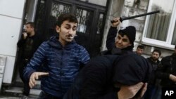 Seorang warga sipil, kiri, dan seorang petugas keamanan memukul seorang pengunjuk rasa saat polisi anti huru-hara menggunakan meriam air untuk membubarkan orang-orang yang berunjuk rasa terhadap penahanan 12 anggota parlemen dari partai pro-Kurdi, HDP (5/11). Istanbul, Turki. (foto: AP Photo/Cagdas Erdogan)