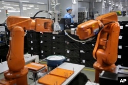 A Chinese worker is seen behind orange robot arms at Rapoo Technology factory in the southern Chinese industrial boomtown of Shenzhen, Aug. 21, 2015. Automation could wipe out two thirds of jobs in some countries, the World Bank warns.