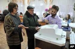 Members of an election commission help a man, center, to cast his ballot in the presidential election in Yekaterinburg, Russia, Sunday, March 18, 2018.