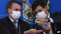 Le ministre brésilien de la santé Luiz Henrique Mandetta appliquant du gel désinfectant sur les mains du président Jair Bolsonaro lors d'une conférence de presse sur le Covid-19, au palais présidentiel Planalto, Brasilia, 18 mars 2019. (Photo AP/André Borges)