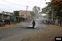 A Kenyan police officer tries to put out flames from a burning tire in Nairobi’s Kibera slum, Aug. 12, 2017. (J. Craig/VOA)