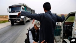 In this March 28, 2018 photo, a Kurdish policeman checks an Arab Syrian man at a checkpoint controlled by The U.S.-backed Syrian Democratic Forces, SDF, on a highway in Hassakeh province.