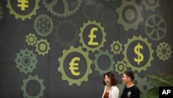 FILE - People walk past a mural on a bank showing symbols for American, Chinese and other world currencies in Beijing, July 7, 2018.