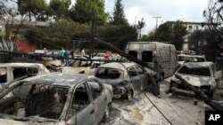 Sekelompok orang berdiri di antara mobil-mobil yang hangus terbakar di Mati, kawasan timur Athena, Selasa, 24 Juli 2018. 