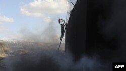 ผู้ประท้วงปีนขึ้นไปปักธงชาติปาเลสไตน์บนกำแพงกั้นระหว่างอิสราเอลกับเขตเวสต์แบงค์ ที่หมู่บ้านบิลินใกล้เมืองรามาลาห์