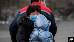 A Chinese families wearing masks ride on a tricycle on a street in Beijing, Feb. 8, 2020.