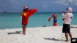 FILE - Chinese tourists take souvenir photos with the Chinese national flag as they visit Quanfu Island, one of Paracel Islands of Sansha prefecture of southern China's Hainan province in the South China Sea, Sept. 14, 2014. 
