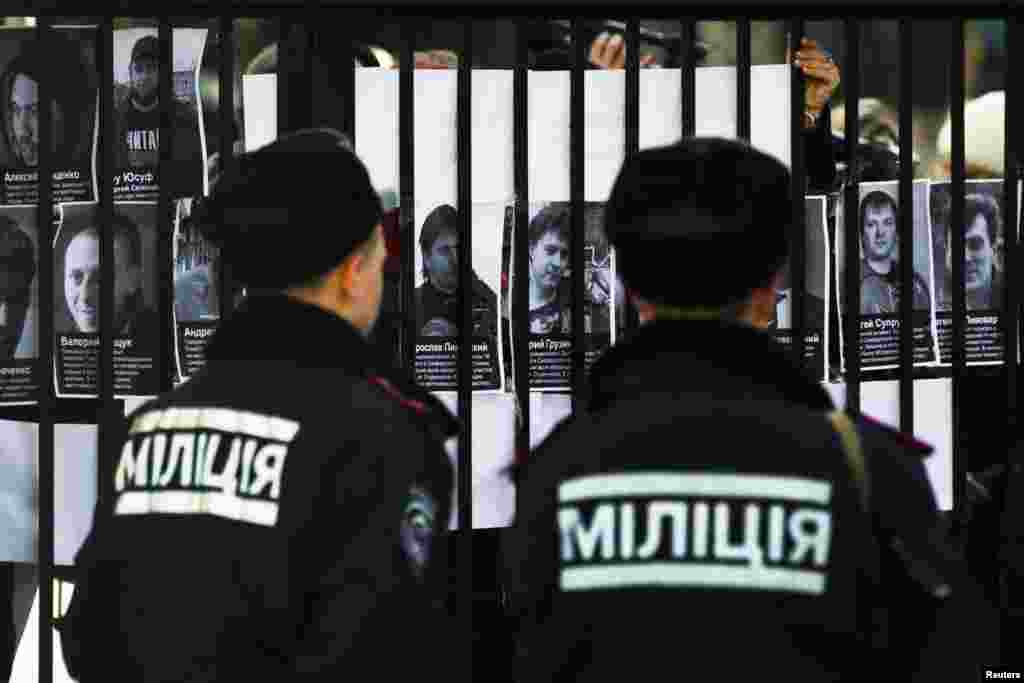Police look at portraits of missing political activists and journalists that protesters pasted on the gate of the Crimean Interior Ministry in Simferopol, March 18, 2014. 