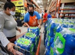 Home Depot department supervisor Arnaldo Gonzalez loads water bottles into Elena Arvalo's shopping cart as shoppers prepare for possible effects of Tropical Storm Elsa in Miami, July 3, 2021.