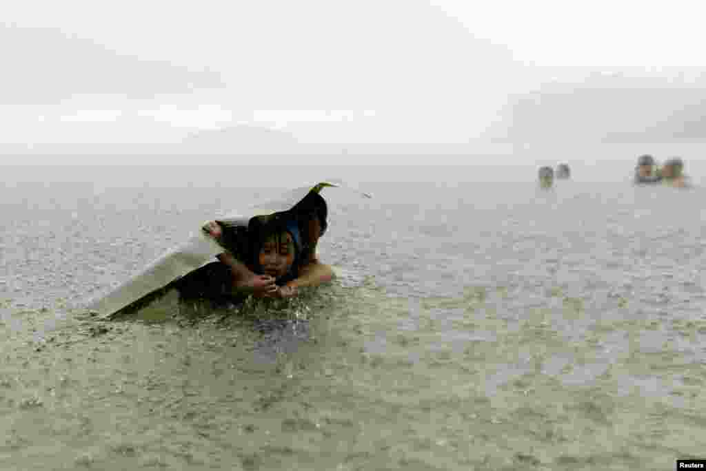 A young girl and a man cover themselves from the rain with a banana leaf in the sea on the outskirts of Colon City, Panama, Oct. 17, 2015.