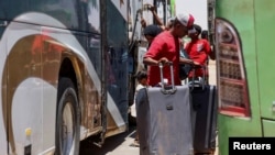 People stand next to buses as passengers fleeing from Sudan arrive at the Argeen land port, after being evacuated from Khartoum to Abu Simbel city, at the upper reaches of the Nile in Aswan