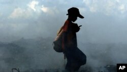 រូប​ឯកសារ៖ ផ្សែង​ហុយ​ត្រលោម​ក្បែរ​ក្មេង​ប្រុស​ម្នាក់ដែលកំពុង​កាយ​រើស​សំរាម ដោយ​សារ​ការ​ដុត​សំរាម​​នៅ​គំនរ​កប់​សំរាម​មួយ​​នៅ​ជាយ​ក្រុង​ភ្នំពេញ កាល​ពី​ថ្ងៃ​ព្រហស្បតិ៍ ទី​១៥ ខែ​មិថុនា ឆ្នាំ២០០៦។ 