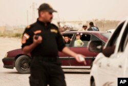 FILE - An Iraqi counter terror officer talks to people in a convoy of families fleeing Islamic State-held Hit, Iraq, at a checkpoint on the western edge of Ramadi, Iraq, March 20, 2016.