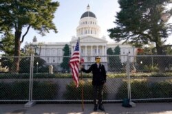 Christian Alvarado holds a U.S. flag in front of a fence surrounding the California Capitol in Sacramento, Jan. 16, 2021. The fence was built because of concerns that protests around Joe Biden's inauguration as president Jan. 20 could turn violent.