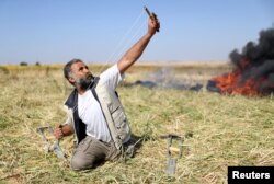 Seorang warga Palestina melemparkan batu kepada pasukan Israel saat bentrokan di perbatasan Gaza-Israel dalam sebuah protes yang menuntut hak mereka kembali ke kampung halaman, di Jalur Gaza selatan, 31 Maret 2018.