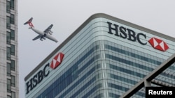 FILE - An aircraft flies past the HSBC headquarters building in the Canary Wharf financial district in east London, Feb. 15, 2015. 