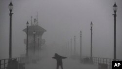 បុរស​ម្នាក់​កំពុង​ដើរ​កាត់​ខ្យល់​បក់​និង​ភ្លៀង​ដ៏​ខ្លាំង​មួយ​នៅ​ផែ Huntington Beach រដ្ឋកាលីហ្វ័រញ៉ា កាល​ពី​ថ្ងៃទី ១៧ កុម្ភៈ ២០១៧។