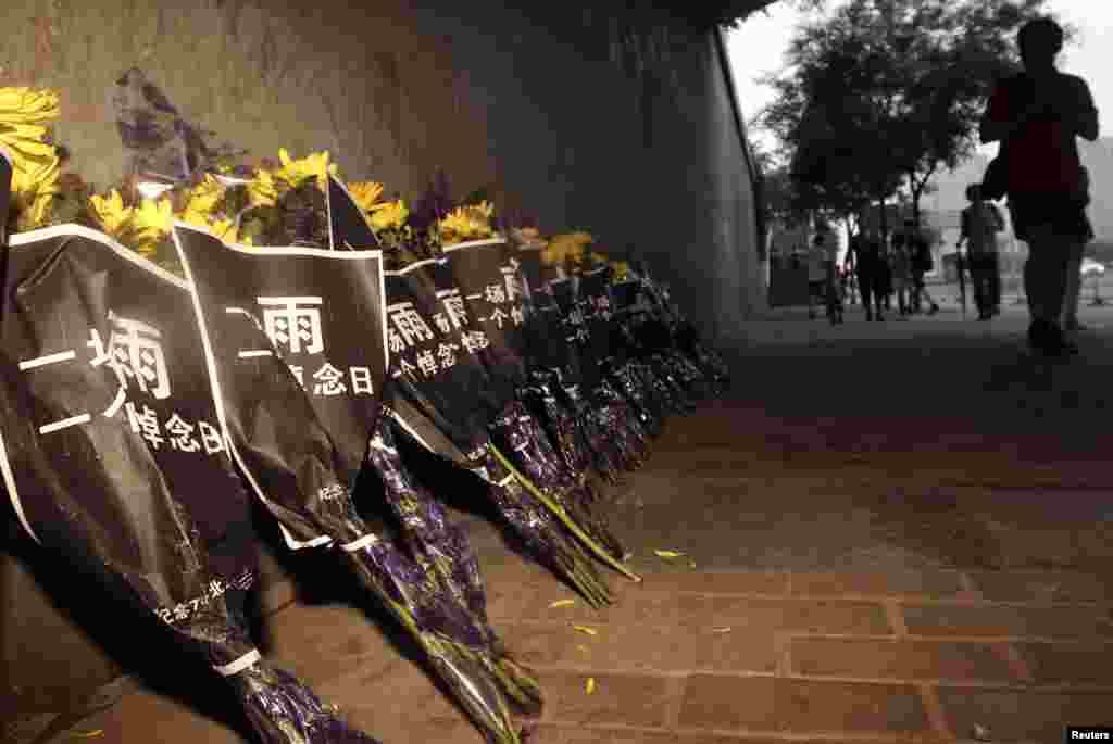 Pedestrians walk past chrysanthemums placed under the Guangqumen overpass to mourn victims who were killed during a rainstorm, in Beijing, China, July 27 2012.