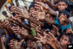Rohingya Muslim children, who crossed over from Myanmar into Bangladesh, stretch their arms out to collect chocolates and milk distributed by Bangladeshi men at Taiy Khali refugee camp, Bangladesh, Sept. 21, 2017.