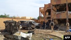 Malian firefighters and soldiers walk beside a destroyed building and burnt cars after a suicide car bomb attack overnight, which killed three people, in Gao, Nov. 13, 2018.