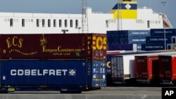 Truck trailers are parked among stacked cargo containers at the Port of Zeebrugge, in Zeebrugge, Belgium, Oct. 24, 2019.