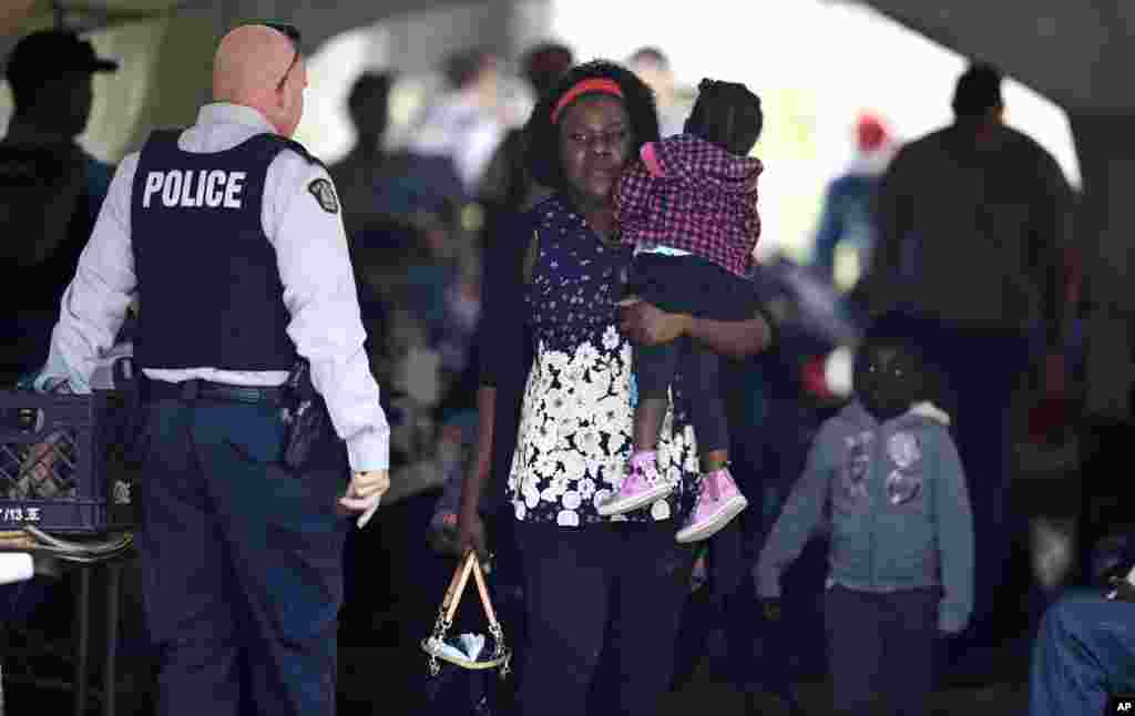 A woman carries a child out of a makeshift police station after crossing illegally into Canada, from the end of Roxham Road in Champlain, New York, in Saint-Bernard-de-Lacolle, Quebec, Aug. 7, 2017.