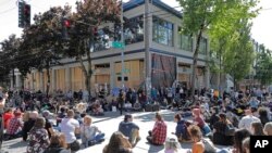 Protesters listen to a speaker as they sit in front of the Seattle Police Department East Precinct building, which has been boarded up and abandoned except for a few officers inside, June 11, 2020.