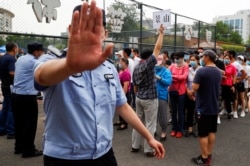 A police officer gestures at a photographer as people line up to get a nucleic acid test at a sport center after a spike of cases of the coronavirus disease (COVID-19), in Beijing, China June 17, 2020. REUTERS/Thomas Peter