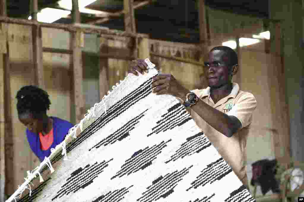 Manager of TEXFAD, John Baptist Okello checks a handmade carpet woven from banana fiber threads, at a factory in Sonde, Mukono District, Uganda, Sept. 20 2023.&nbsp;