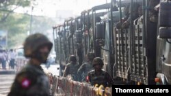 Soldiers stand next to military vehicles as people gather to protest against the military coup, in Yangon on June 2021.