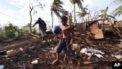 Samuel and his father, Phillip, at back, pick through the debris of their house in Port Vila, Vanuatu in the aftermath of Cyclone Pam Monday, March 16, 2015. (AP Photo/Dave Hunt, Pool)