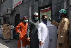 FILE - A man checks the body temperature of worshippers arriving for Friday prayers at a mosque in Lahore, Pakistan, May 1, 2020.
