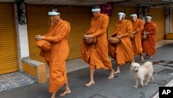 Thai Buddhist monks wear face shields to protect themselves from new coronavirus as they walk to collect alms from devotees in Bangkok, Thailand, Tuesday, March 31, 2020. 