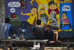 Orang-orang duduk di depan mural kampanye pemilihan umum Indonesia menjelang pemilihan bulan depan di Banda Aceh, Aceh pada 17 Maret 2019. (Foto: AFP/Chaideer Mahyuddin)