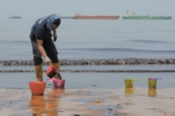 Seorang polisi menyendoki minyak yang mencemari Pantai Banua Patra dari tumpahan minyak di perairan Balikpapan, Kalimantan Timur, 2 April 2018. (Foto: Antara/Sheravim via REUTERS)