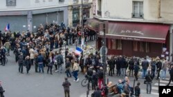People stand in front of the restaurant Le Carillon and Le Petit Cambodge, the both establishments targeted in Friday's gun and bomb attacks, in Paris, Monday, Nov. 16, 2015. French police raided more than 150 locations overnight as authorities released the names of two more potential suicide bombers involved in the Paris attacks— one born in Syria, the other a Frenchman wanted as part of a terrorism investigation. (AP Photo/Kamil Zihnioglu)