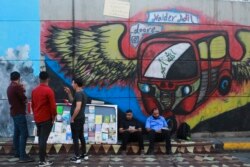 In this Sunday, Nov. 17, 2019 photo, protesters read donated books in front of graffiti, at the Saadoun Tunnel, in Baghdad, Iraq. The tunnel that passes under Baghdad’s landmark Tahrir Square has become an ad hoc museum for Iraq's revolution: Young artist