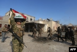 A member of the Iraqi security forces raise the Iraqi flag in the Anbar police headquarters after their entry into the center of Ramadi, the capital of Iraq's Anbar province, about 110 kilometers west of Baghdad, Dec. 28, 2015.